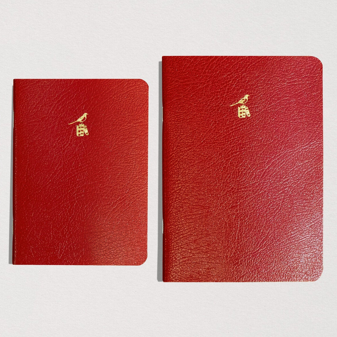Three red leather notebooks with gold embossed logos on a light gray background