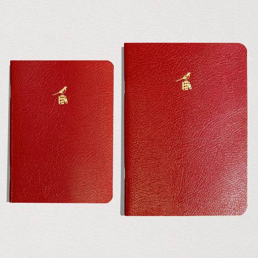 Three red leather notebooks with gold embossed logos on a light gray background