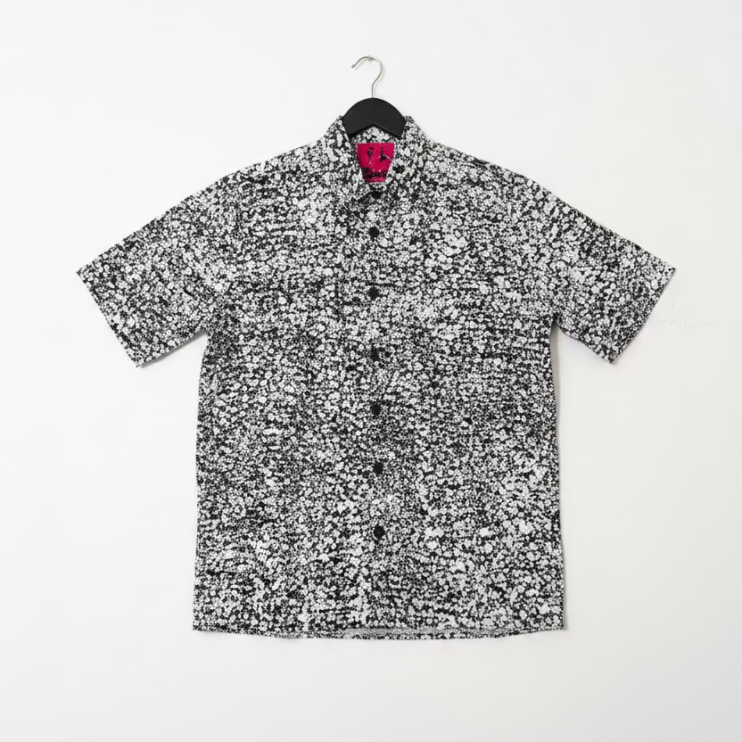 Short-sleeve shirt with black and white pattern on a hanger against a white wall.