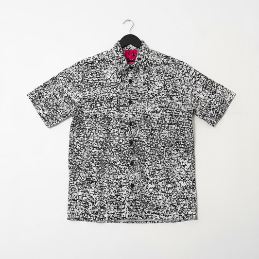 Short-sleeve shirt with black and white pattern on a hanger against a white wall.