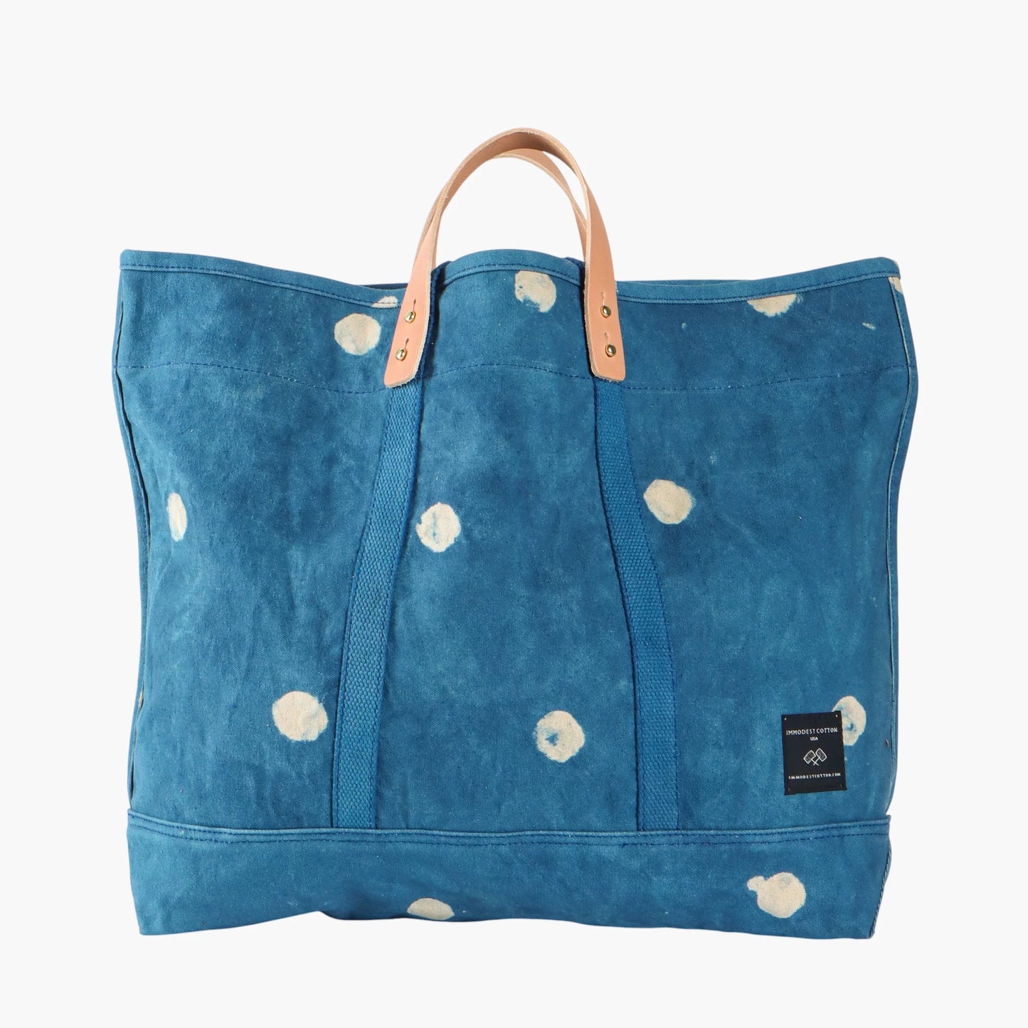 Blue tote bag with white floral patterns and brown handles on a white background
